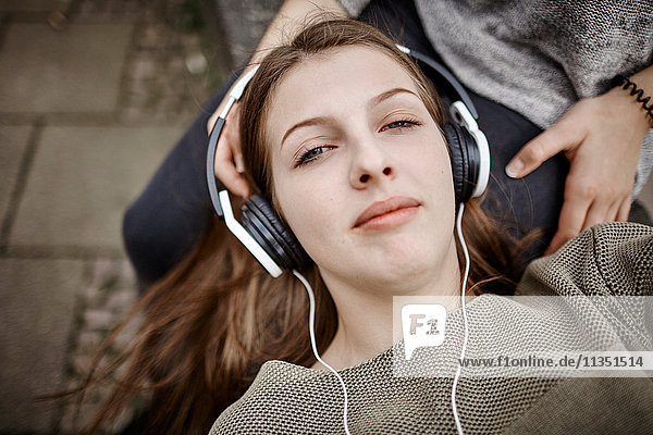 Entspannte junge Frau mit Kopfhörern liegt auf dem Schoß ihrer Freundin