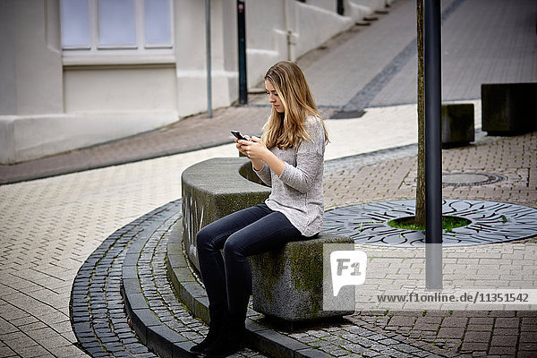 Sitzende junge Frau schaut auf ihr Handy