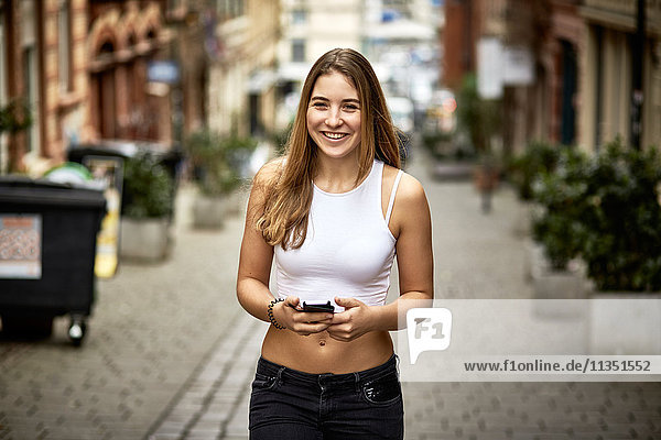 Portrait einer lächelnden jungen Frau mit Handy in der Stadt