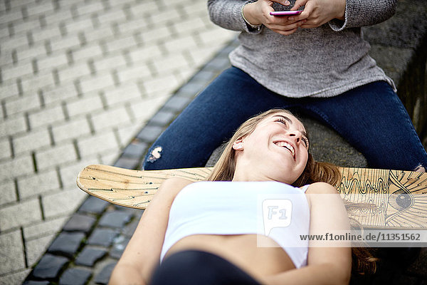 Zwei fröhliche junge Frauen mit Handy und Skateboard