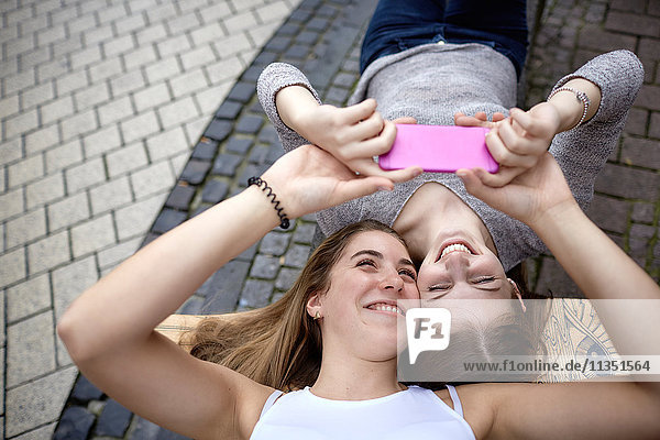 Two happy young women lying on skateboard taking a selfie