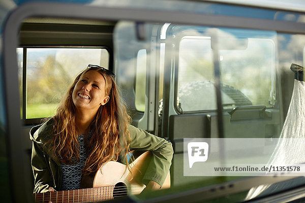 Young woman playing guitar in car