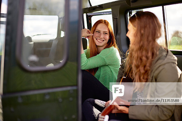 Lächelnde junge Frau schaut auf ihre Freundin mit Gitarre im Auto