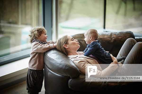 Mutter und Baby liegen auf der Couch und werden von der Tochter beobachtet