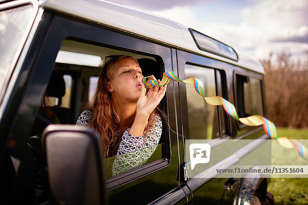 Young woman blowing paper streamer out of car window