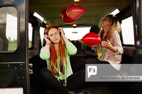 Two young women in car with headphones and balloons