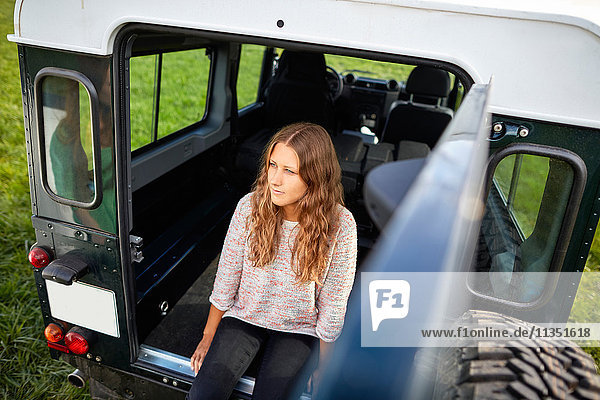 Junge Frau sitzt im Kofferraum eines Geländewagens auf einer Wiese geparkt