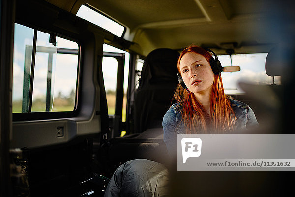 Young woman with sleeping bag and headphones in off-road vehicle