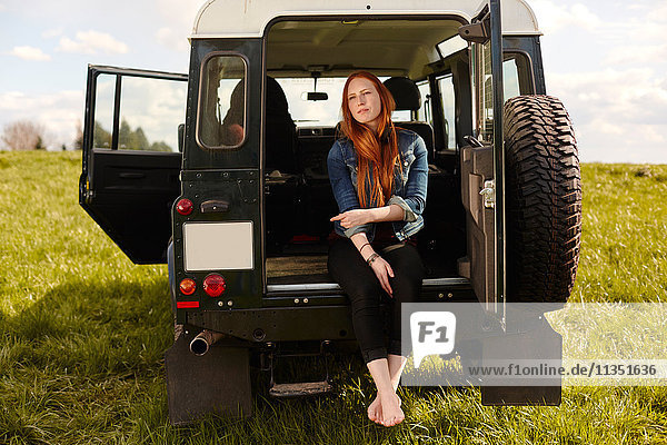Young woman sitting in trunk of off-road vehicle parked on a meadow