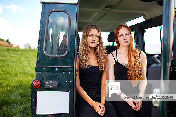Zwei junge Frauen sitzen im Kofferraum eines Geländewagens auf einer Wiese