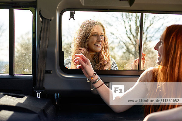 Lächelnde junge Frau im Auto mit Freundin hinter dem Fenster