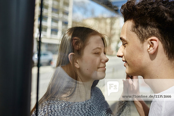 Teenage couple looking at each other through glass pane