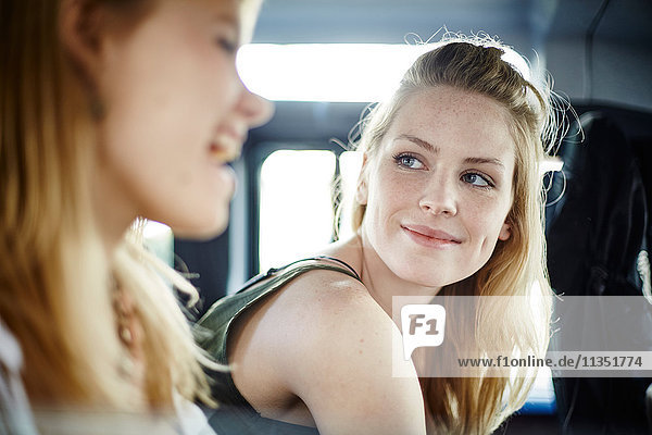 Lächelnde junge Frau im Auto schaut ihre Freundin an