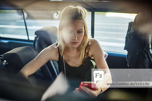 Young woman in car with earbud and cell phone
