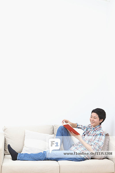 Young Japanese man reading book on the sofa