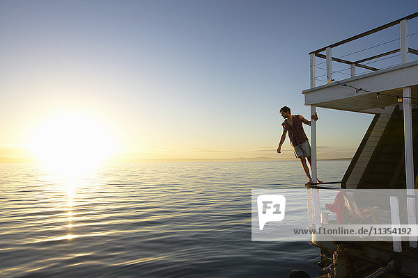 Mann stützt sich auf Sommerhausboot-Geländer über Sonnenuntergang Ozean