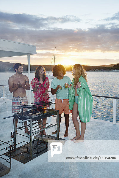 Young adult friends barbecuing  hanging out and drinking on summer houseboat at sunset