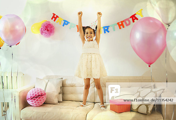 Portrait selbstbewusstes Mädchen mit erhobenen Armen auf dem Sofa bei der Geburtstagsfeier