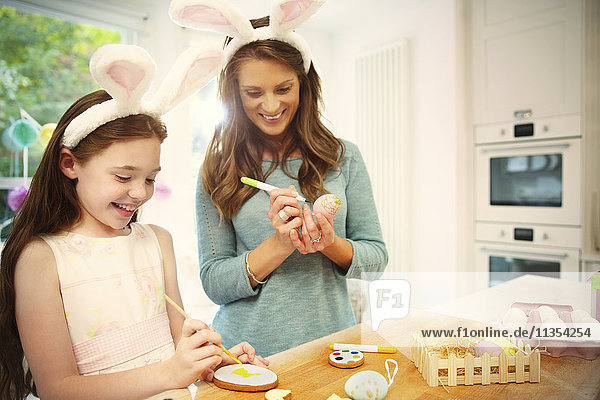 Mother and daughter wearing costume rabbit ears coloring Easter eggs and cookies
