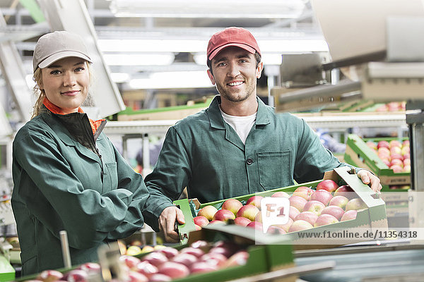 Portrait lächelnde Arbeiter mit Schachteln mit roten Äpfeln im Lebensmittelbetrieb