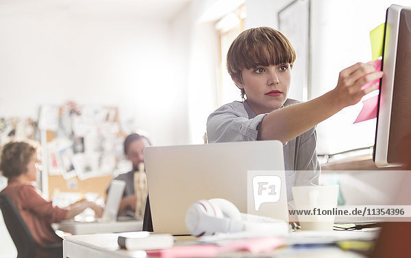 Serious female designer reviewing adhesive notes on computer in office