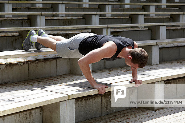 Junger Mann trainiert  macht Push-Ups auf der Stadiontreppe