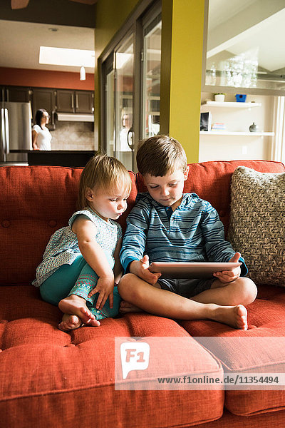 Siblings using digital tablet on sofa