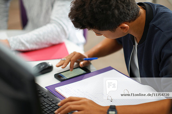 Junge männliche College-Studenten am Computerschreibtisch beim Rechnen mit einem Smartphone