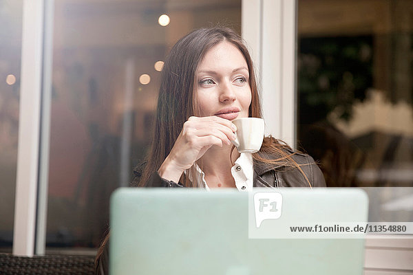 Geschäftsfrau mit Laptop trinkt Espresso im Straßencafé