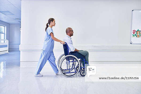 Arzt im Krankenhaus schiebt Patient im Rollstuhl