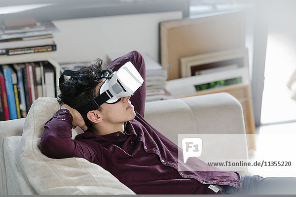 Junger Mann auf Sofa mit Virtual-Reality-Headset