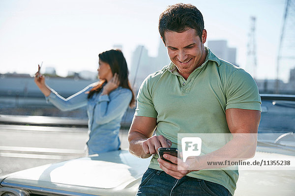 Couple by car using smartphones  Los Angeles  California  USA