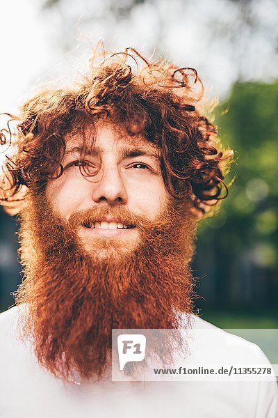 Porträt eines jungen männlichen Hipsters mit lockigem roten Haar und Bart im Park