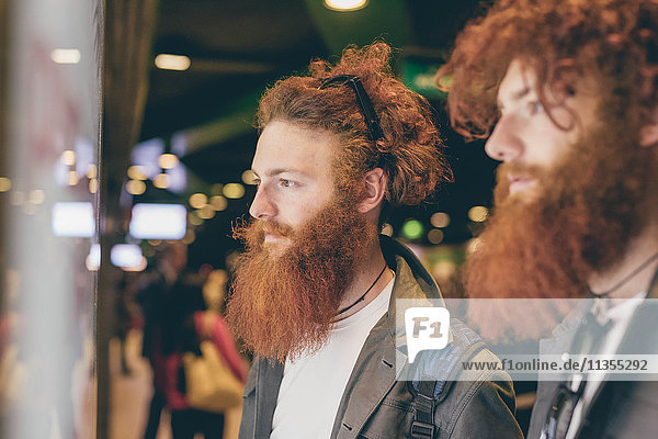 Young male hipster twins with red hair and beards window shopping at night