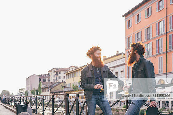 Junge männliche Hipster-Zwillinge mit roten Haaren und Bärten  die am Kanalufer sprechen.