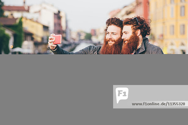 Junge männliche Hipster-Zwillinge mit roten Haaren und Bärten  die Smartphone Selfie am Kanalufer nehmen