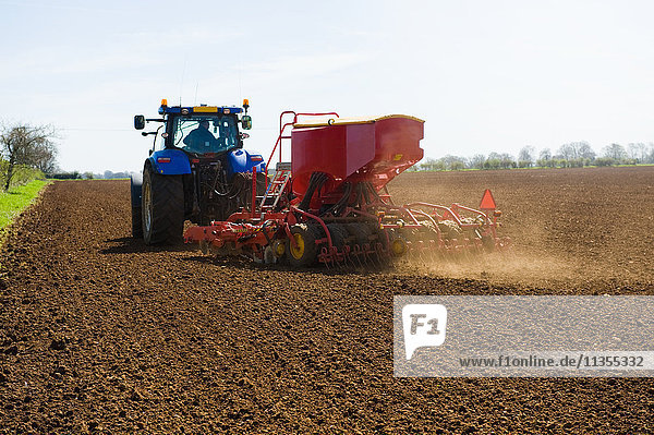 Farm tractor and seed drill sowing ploughed field in spring
