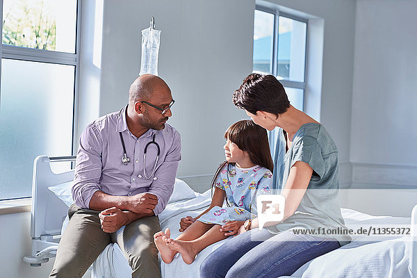Männlicher Arzt im Gespräch mit Patientin und ihrer Mutter auf der Kinderstation im Krankenhaus
