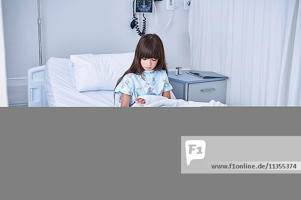 Patientin im Bett  die in der Kinderabteilung des Krankenhauses auf den Gipsarm schaut