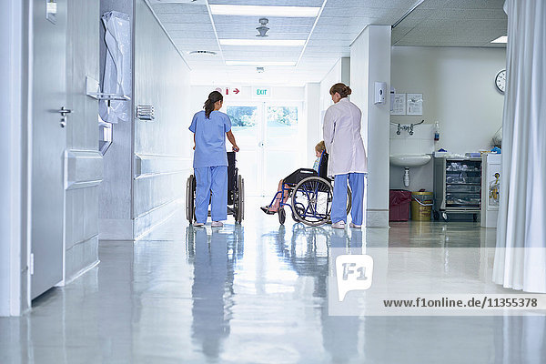 Rear view of medical orderly pushing child patient in wheelchair on hospital children's ward
