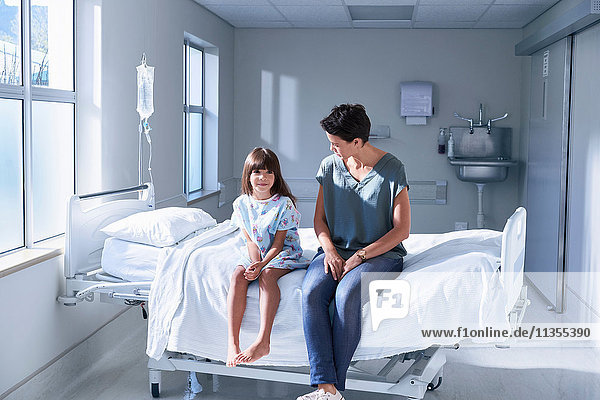 Girl patient and her mother sitting on bed in hospital children's ward