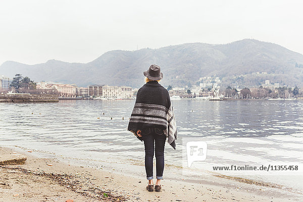 Rückansicht einer stilvollen jungen Frau  die vom Seeufer aus auf den Comer See schaut  Comer See  Italien
