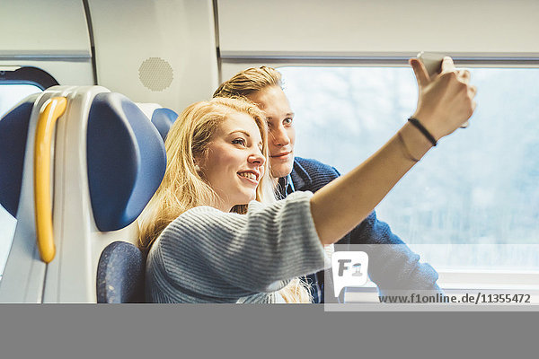 Young couple taking smartphone selfie in train carriage