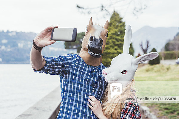 Couple wearing horse and rabbit masks taking smartphone selfie  Lake Como  Italy