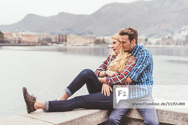 Romantic young couple sitting on harbour wall  Lake Como  Italy