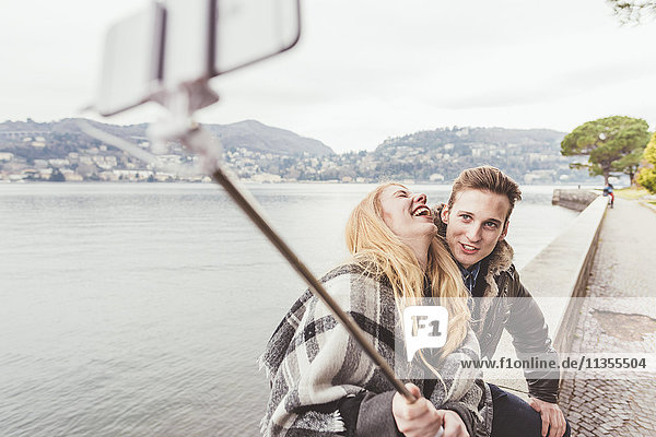 Young couple laughing taking smartphone selfie on harbour wall  Lake Como  Italy
