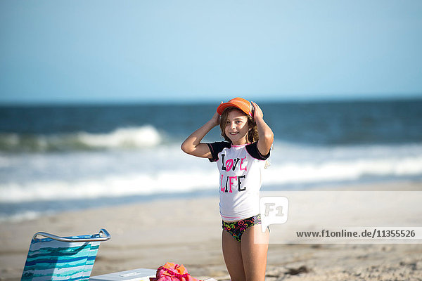 Young girl on beach putting cap on