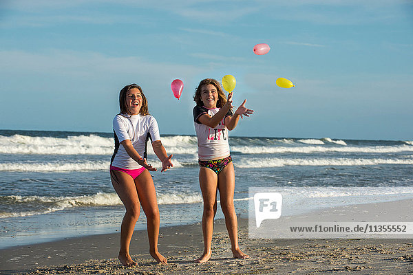 Zwei junge Schwestern spielen mit kleinen Luftballons am Strand