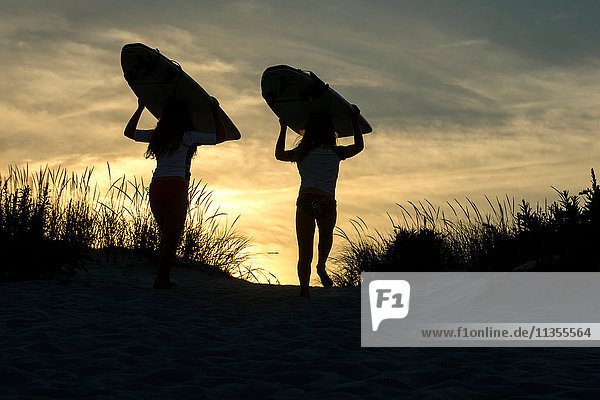 Zwei junge Mädchen auf Sanddünen  in der Abenddämmerung  mit Surfbrettern