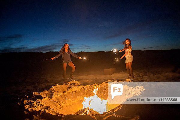 Zwei junge Mädchen halten am Strand am Lagerfeuer Wunderkerzen und halten Wunderkerzen